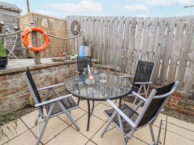 A patio with four black mesh chairs around a glass table with a bottle and four glasses by a wooden fence at Sea Shore in Seahouses