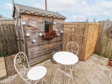 A small garden patio with a wooden shed a round white metal table and two matching chairs at Sea Shore in Seahouses