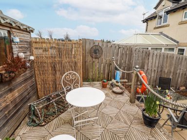 A small wooden patio with a white round table and chair a fishing net a planter and a life ring at Sea Shore in Seahouses