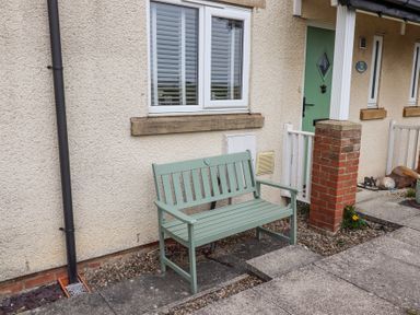 A green bench outside a house with a green door and a brick pillar at Sea Shore in Seahouses