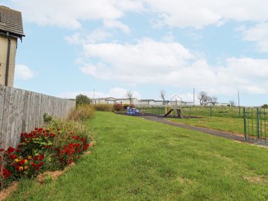 A playground with a slide and climbing frame on grass near a wooden fence and flowers at Sea Shore in Seahouses
