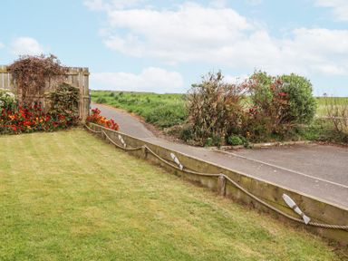 A garden lawn with a wooden fence, red flowers, bushes, and a paved path at Sea Shore in Seahouses