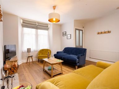 A living room with a blue sofa a yellow armchair a wooden coffee table and a television at Bellflower Cottage in Windermere