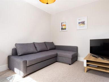 A gray sectional sofa a wooden TV stand with a TV and two framed pictures on the wall at Bellflower Cottage in Windermere