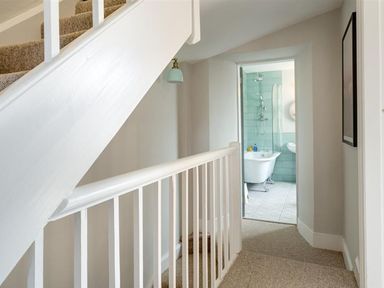 A staircase with carpet leading to a hallway and a bathroom with a clawfoot bathtub and green tiles at Bellflower Cottage in Windermere