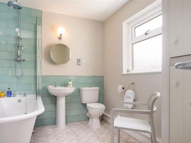 A bathroom with a bathtub shower sink toilet round mirror chair and window at Bellflower Cottage in Windermere