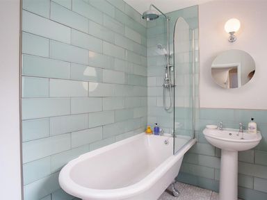 A bathroom with a bathtub shower combination a pedestal sink round mirror and light fixture at Bellflower Cottage in Windermere