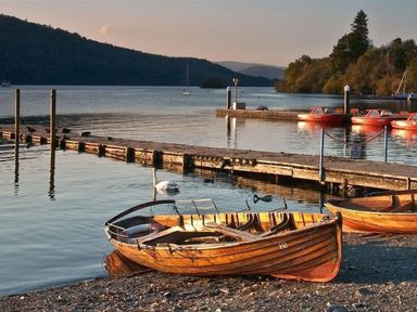 A lakeside scene with wooden rowboats on the shore a wooden dock and red boats on the water at Bellflower Cottage in Windermere
