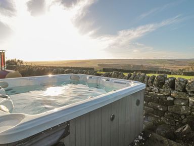 An outdoor hot tub near a stone wall with rolling hills in the background at Petty Knowes Cottage Rochester near Otterburn