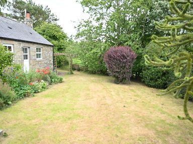 A garden with a stone house and various plants at Petty Knowes Cottage Rochester near Otterburn