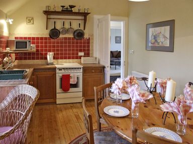 A kitchen with wooden cabinets red tiled backsplash stove and a dining table set with plates candles and napkins at Bank View in Chirnside