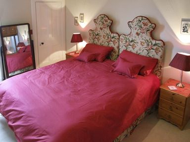 A bedroom with a double bed with a red bedspread and floral headboards two bedside tables with lamps and a standing mirror at Bank View in Chirnside