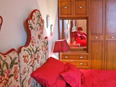 A bedroom with a floral headboard red bedding and a wooden wardrobe with a mirror at Bank View in Chirnside