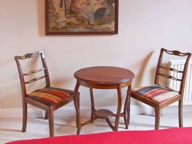A wooden round table with two wooden chairs with striped cushions in a room at Bank View in Chirnside