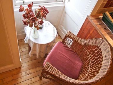 A wicker chair with a cushion next to a small round table with dried flowers in a vase at Bank View in Chirnside