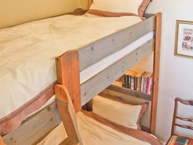 A bedroom with wooden bunk beds a small bookshelf with books and a framed picture on the wall at Bank View in Chirnside