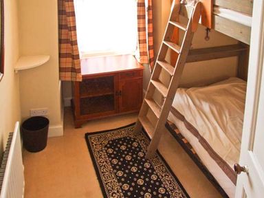 A small bedroom with a bunk bed a wooden cabinet under a window and a patterned rug on the floor at Bank View in Chirnside