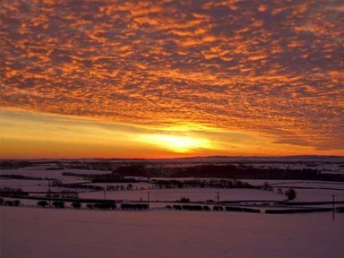 A snowy rural landscape with a sunset and orange clouds in the sky at Bank View in Chirnside