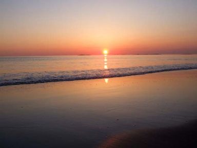 A beach with waves and a sun setting over the ocean