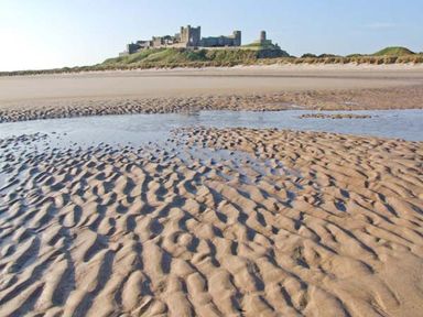 A sandy beach with ripples and water pools with a castle on a hill in the background