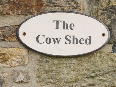 An oval sign with The Cow Shed mounted on a stone wall at Cowshed in Normanby near Flyingthorpe