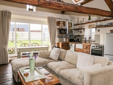 A living area with a beige sofa a wooden coffee table a dining table and a kitchen with wooden cabinets at Cowshed Normanby near Flyingthorpe