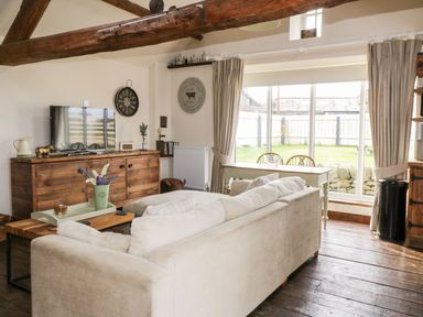 A living room with a white couch a wooden TV cabinet and a dining table near glass doors at Cowshed Normanby near Flyingthorpe
