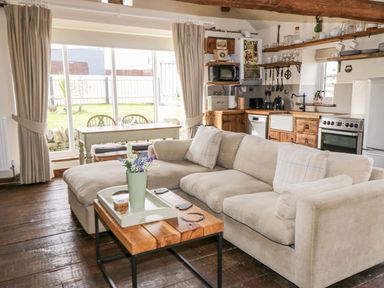 A living room with a beige sofa and wooden coffee table next to a kitchen with wooden cabinets and dining table at Cowshed Normanby near Flyingthorpe