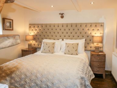A bedroom with a large tufted headboard a bed with pillows and two bedside tables with lamps at Cowshed Normanby near Flyingthorpe