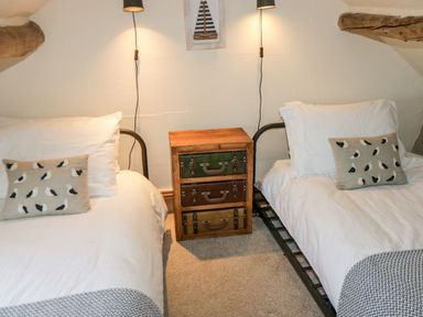 A bedroom with two single beds a wooden nightstand and wall lamps at Cowshed Normanby near Flyingthorpe