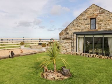 A stone house with large windows and a garden with a small palm tree and decorative chickens at Cowshed Normanby near Flyingthorpe