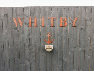 A wooden fence with the word Whitby an anchor and a small basin mounted on it