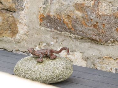 A small metal lizard sculpture on a stone with a stone wall in the background at Cowshed Normanby near Flyingthorpe