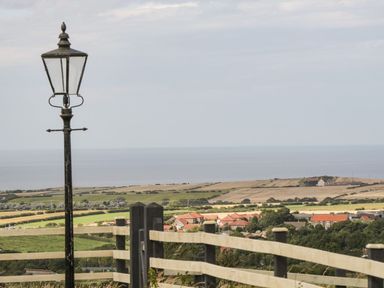 A lamp post near a wooden fence overlooking a rural landscape with fields and houses near the sea at Cowshed Normanby near Flyingthorpe