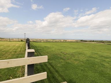 A fenced grassy field with a lamppost under a cloudy sky at Cowshed in Normanby near Flyingthorpe