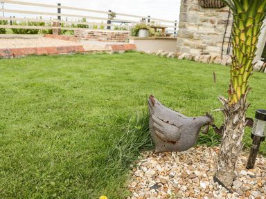 A garden with grass a metal chicken decoration a palm tree and a stone wall at Cowshed Normanby near Flyingthorpe