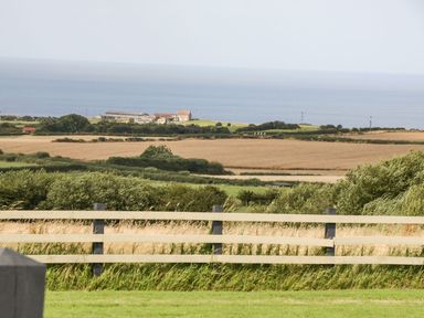 A rural landscape with fields trees and a wooden fence overlooking the sea at Cowshed Normanby near Flyingthorpe
