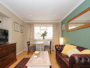 A living room with a brown leather sofa yellow cushions a wooden coffee table a small dining table with two chairs and a wooden dresser at Alway in Lifton