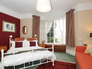 A bedroom with a white metal bed frame red pillows patterned curtains and a window seat at Alway in Lifton