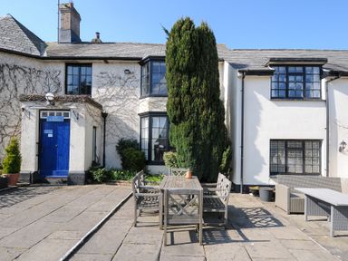 An outdoor patio area with wooden table and chairs in front of a white building with black window frames at Alway in Lifton