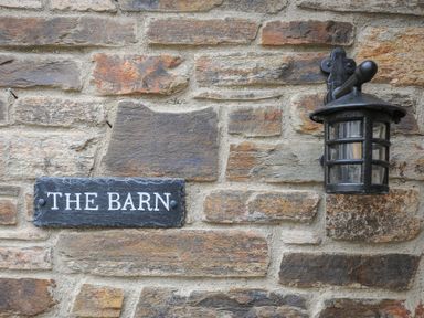 A stone wall with a black lantern and a sign that reads The Barn at The Barn in Lifton