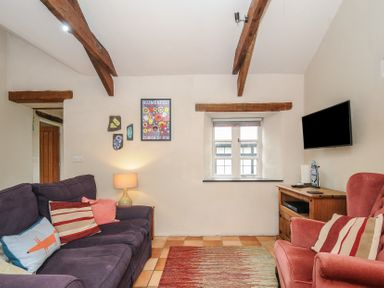 A living room with a purple sofa and a red armchair a wooden cabinet with a wall mounted TV and wooden ceiling beams at The Barn in Lifton