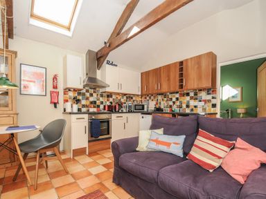 A kitchen with tiled backsplash white and wood cabinets and a purple sofa with cushions at The Barn in Lifton