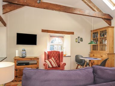 A living room with a purple sofa a red armchair a wooden cabinet and a dining table with chairs at The Barn in Lifton