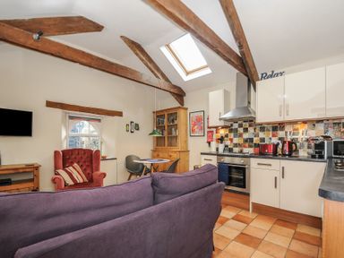 An open plan kitchen and living area with wooden beams tiled floor and skylight at The Barn Lifton