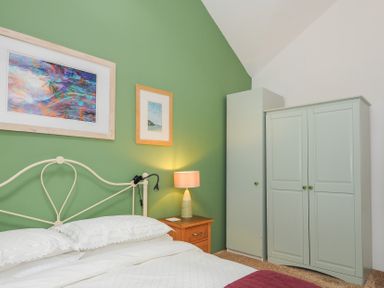 A bedroom with a bed a wooden nightstand with a lamp two wardrobes and framed pictures on a green wall at The Barn in Lifton