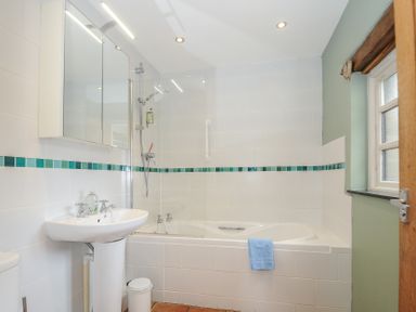 A bathroom with a bathtub shower combination sink with mirror cabinet and window at The Barn in Lifton