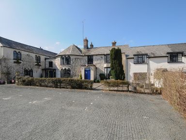 A front view of a white building with arched windows and a blue door with a paved parking area in front at The Barn in Lifton