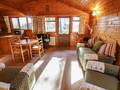 A wooden cabin living room with green upholstered sofas a round wooden dining table and kitchen appliances at Goldcrest in Withern near Alford