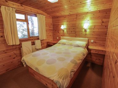 A bedroom with a bed placed against wooden walls under two wall lamps and a window with curtains at Goldcrest in Withern near Alford